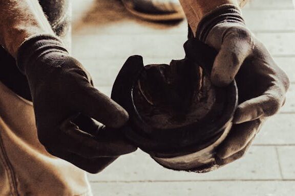 Man Hands in Glove Holding Horse Leg with Horseshoe